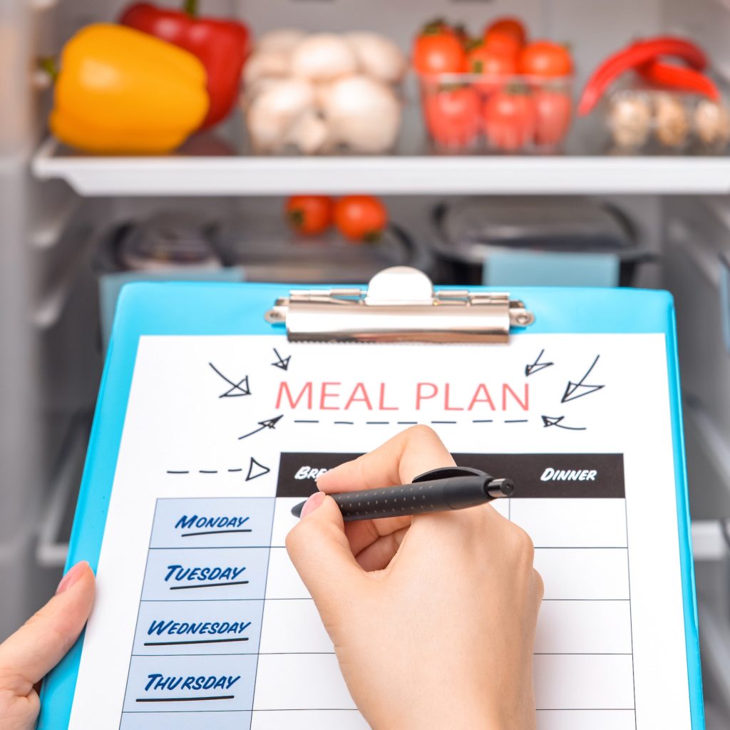 Person holding a clipboard with the words "Meal Plan" in front of an open fridge