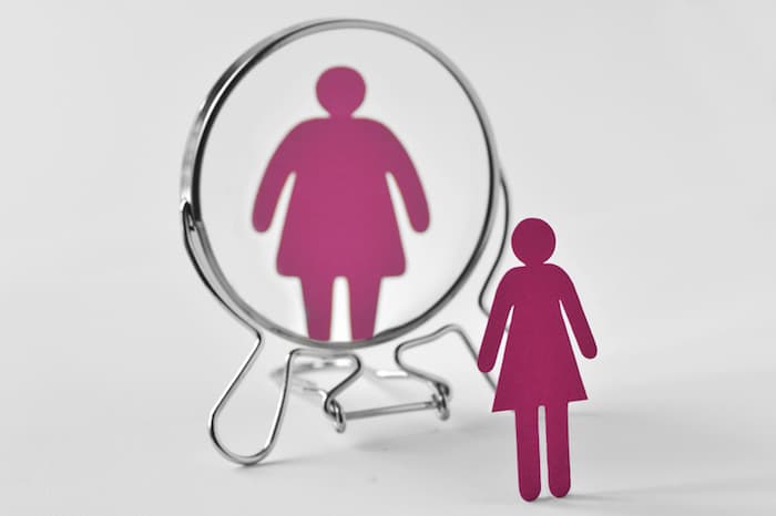 A paper icon of a woman looking in the mirror and her reflection is distorted to look fatter than she is in reality