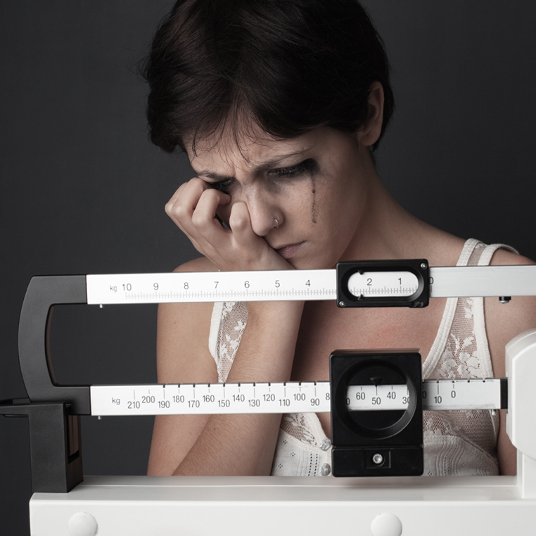 Woman crying while weighing herself on a scale