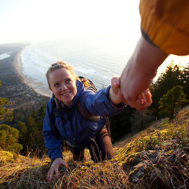 Woman climbing a hill with assistance from someone at the top